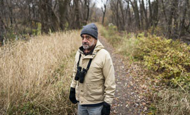 Man walking a trail in the woods with binoculars around his neck