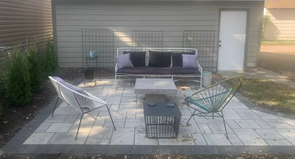 Gray paver patio with a loveseat, wire chairs and a fire pit table beside a garage in a Bloomington, MN backyard