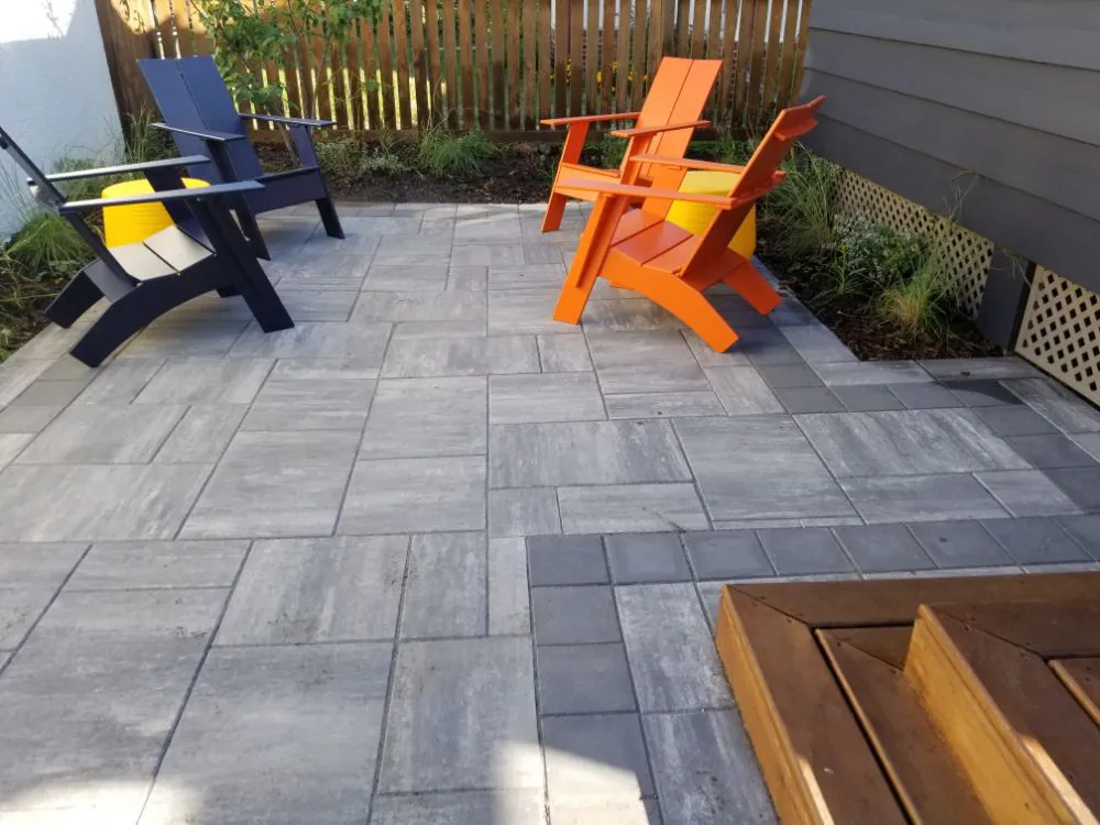 Gray paver patio with navy and orange Adirondack-style chairs beside a wood bench and cedar fence in Eagan, MN
