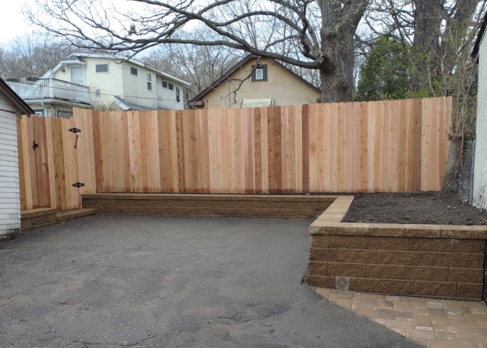 Cedar privacy fence above a low stone retaining wall bordering a gravel patio in an Edina, MN backyard